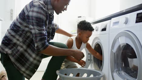 Side-view-of-black-father-and-son-washing-clothes-in-washing-machine-at-comfortable-home-4k