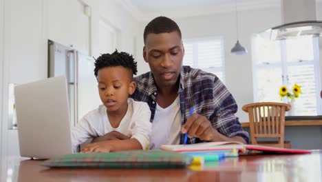Vorderansicht-Eines-Schwarzen-Vaters,-Der-Seinem-Sohn-Bei-Den-Hausaufgaben-In-Einem-Komfortablen-Zuhause-Hilft,-4k