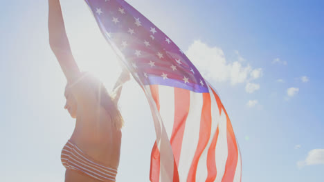 Side-view-of-young-Caucasian-woman-holding-a-American-flag-on-the-beach-4k