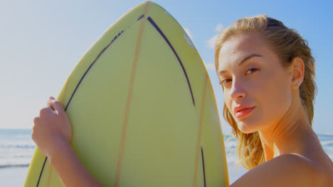 Side-view-of-young-Caucasian-woman-standing-with-surfboard-on-the-beach-4k