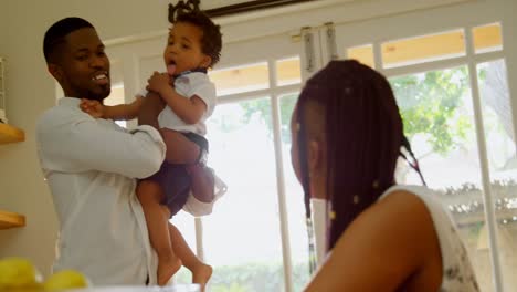 Front-view-of-young-black-father-holding-his-son-and-talking-with-mother-in-kitchen-at-home-4k