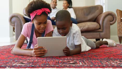 Vorderansicht-Von-Schwarzen-Kindern,-Die-Auf-Dem-Boden-Liegen-Und-Ein-Digitales-Tablet-In-Einem-Komfortablen-Zuhause-Nutzen,-4K