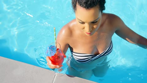 High-angle-view-of-young-mixed-race-woman-walking-with-cocktail-glass-in-swimming-pool-4k