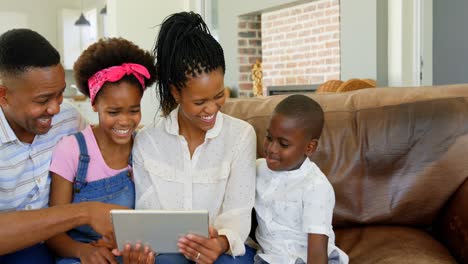Vorderansicht-Einer-Schwarzen-Familie,-Die-Auf-Der-Couch-Sitzt-Und-Ein-Digitales-Tablet-In-Einem-Komfortablen-Zuhause-Nutzt,-4K