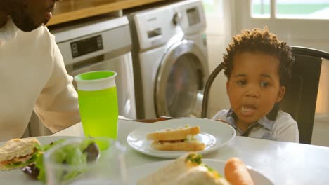 Front-view-of-cute-little-black-son-eating-food-at-dinning-table-in-kitchen-of-comfortable-home-4k