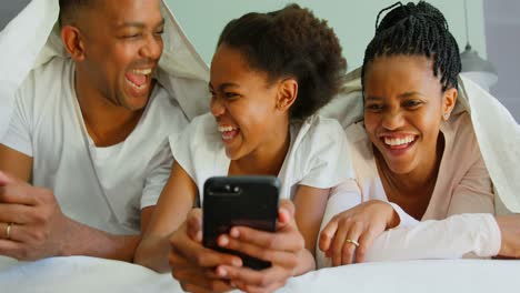 Vorderansicht-Einer-Glücklichen-Schwarzen-Familie,-Die-Ihr-Mobiltelefon-Auf-Dem-Bett-In-Einem-Komfortablen-Zuhause-Nutzt,-4K