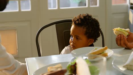 Front-view-of-cute-little-black-son-eating-food-at-dinning-table-in-kitchen-of-comfortable-home-4k