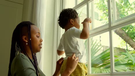 Side-view-of-young-black-mother-playing-with-his-son-on-window-sill-in-a-comfortable-home-4k
