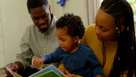 Front-view-of-young-black-parents-and-son-reading-a-story-book-and-sitting-on-floor-at-home-4k
