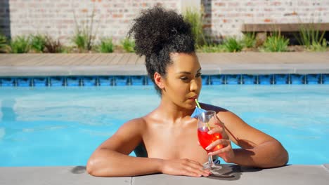 Front-view-of-young-mixed-race-woman-drinking-cocktail-in-swimming-pool-4k