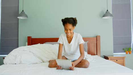 Vorderansicht-Eines-Schwarzen-Mädchens,-Das-Auf-Dem-Bett-Sitzt-Und-Ein-Digitales-Tablet-In-Einem-Komfortablen-Zuhause-Nutzt,-4K