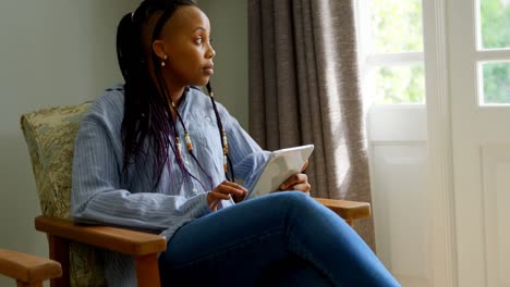 Side-view-of-young-black-woman-using-digital-tablet-and-sitting-on-the-couch-in-comfortable-home-4k