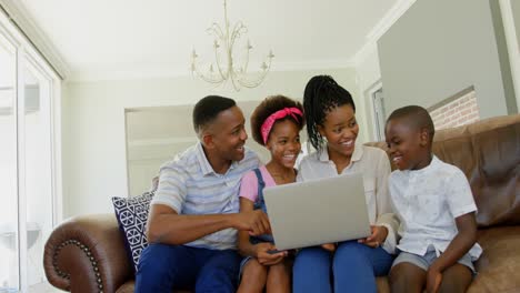 Vorderansicht-Einer-Jungen-Schwarzen-Familie,-Die-Auf-Der-Couch-Sitzt-Und-Einen-Laptop-In-Einem-Komfortablen-Zuhause-Benutzt,-4K