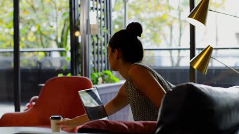 Side-view-of-young-caucasian-female-executive-working-on-laptop-and-drinking-coffee-in-modern-office