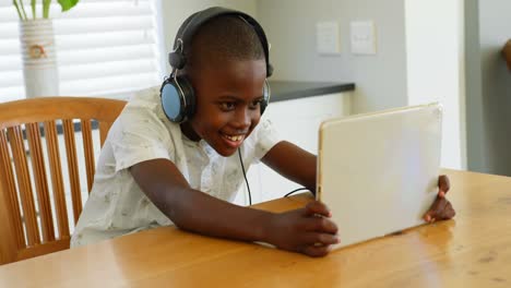 Vista-Frontal-De-Un-Niño-Negro-Jugando-En-Una-Tableta-Digital-En-La-Mesa-Del-Comedor-En-Una-Cómoda-Casa-4k