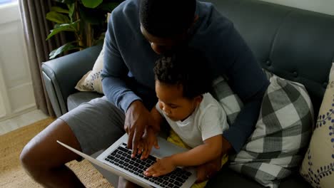 High-angle-view-of-young-black-father-and-son-using-laptop-in-living-room-of-comfortable-home-4k