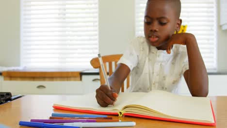 Front-view-of-little-black-boy-doing-homework-at-dining-table-in-a-comfortable-home-4k