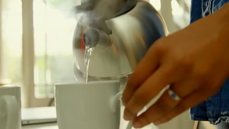 Close-up-of-black-woman-pouring-hot-water-in-coffee-cup-at-dinning-table-in-kitchen-4k