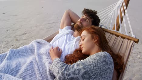Front-view-of-young-romantic-caucasian-couple-sleeping-in-hammock-at-beach-on-a-sunny-day-4k