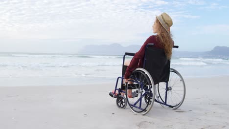 Rückansicht-Einer-Jungen-Behinderten-Kaukasischen-Frau-Mit-Hut,-Die-Im-Rollstuhl-Am-Strand-Sitzt-4k
