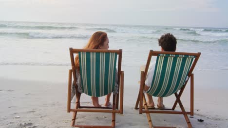 Rückansicht-Eines-Jungen-Kaukasischen-Paares,-Das-Sich-An-Einem-Sonnigen-Tag-Auf-Einer-Sonnenliege-Am-Strand-Entspannt-4k