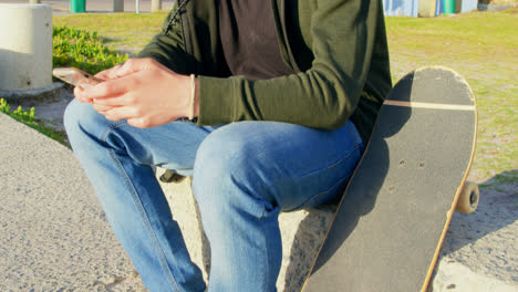 Seitenansicht-Eines-Jungen-Kaukasischen-Mannes,-Der-Auf-Dem-Bürgersteig-Sitzt-Und-SMS-Auf-Dem-Mobiltelefon-Schreibt-4k