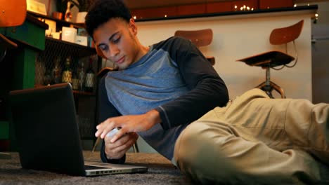 Front-view-of-mixed-race-young-man-using-mobile-phone-while-working-on-laptop-in-a-home-4k