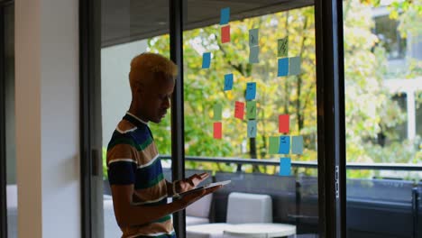 Side-view-of-young-mixed-race-male-executive-looking-at-sticky-note-while-working-on-digital-tablet-