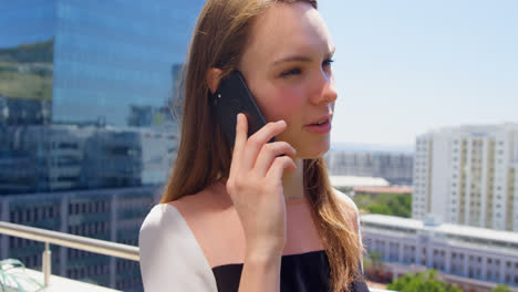 Side-view-of-young-caucasian-businesswoman-talking-on-mobile-phone-in-balcony-of-modern-office-4k