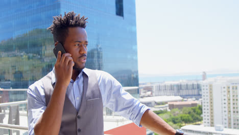 Front-view-of-young-black-businessman-talking-on-mobile-phone-in-balcony-of-modern-office-4k