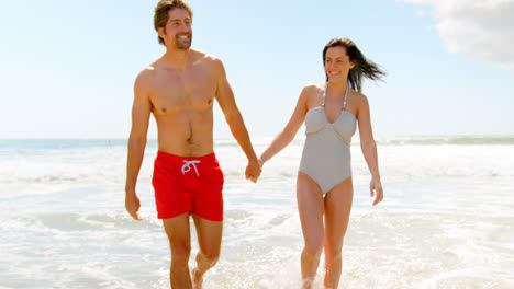 Front-view-of-young-caucasian-couple-walking-hand-in-hand-at-beach-4k