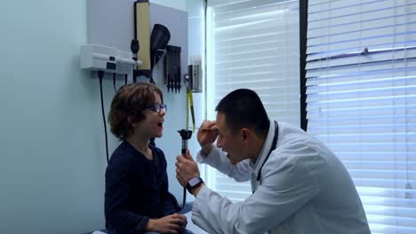 Side-view-of-young-asian-male-doctor-examining-caucasian-boy-patient-with-tool-in-a-clinic-4k
