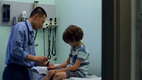Side-view-of-young-asian-male-doctor-examining-caucasian-boy-patient-hand-in-a-clinic-4k