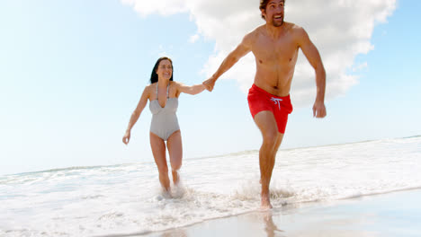 Front-view-of-young-caucasian-couple-running-with-hand-in-hand-at-beach-4k