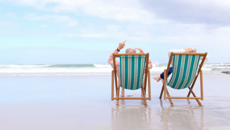 Rear-view-of-old-caucasian-senior-couple-sitting-on-sun-lounger-and-holding-hands-at-beach-4kRear-vi