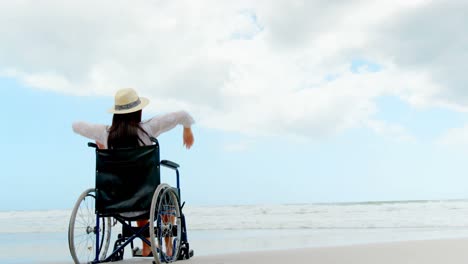 Vista-Trasera-De-Una-Mujer-Discapacitada-Sentada-Con-Los-Brazos-Arriba-En-Silla-De-Ruedas-En-La-Playa-4k