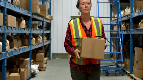 Front-view-of-caucasian-female-worker-walking-with-cardboard-box-in-factory-4k