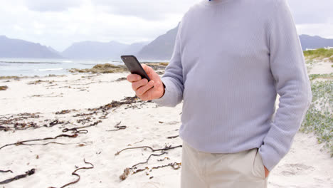 Mid-section-of-old-caucasian-senior-man-using-mobile-phone-at-beach-4k