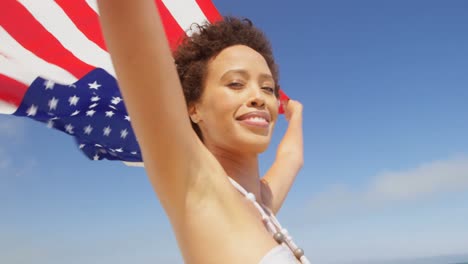 Mujer-Parada-Junto-Al-Mar-Con-Una-Bandera-Americana-Ondeando.-En-La-Playa-4k