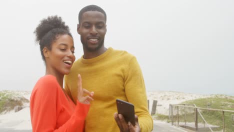 Vorderansicht-Eines-Jungen-Schwarzen-Paares,-Das-An-Einem-Sonnigen-Tag-Am-Strand-Mit-Dem-Mobiltelefon-Auf-Ein-Selfie-Klickt,-4K