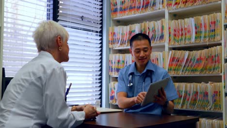 Young-Asian-male-doctor-and-senior-patient-discussing-over-digital-tablet-in-the-clinic-4k
