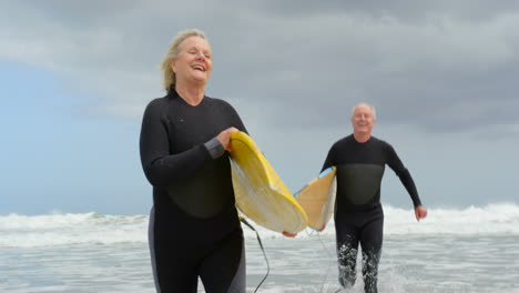 Front-view-of-old-caucasian-senior-couple-running-with-surfboard-at-beach-4k