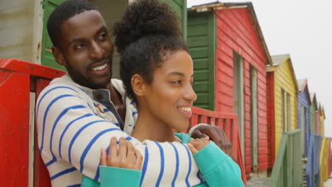 Side-view-of-young-black-couple-embracing-and-looking-at-sea-while-sitting-at-beach-hut-4k