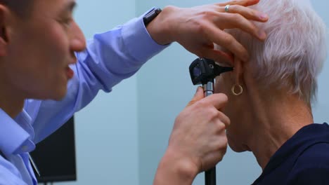 Young-Asian-male-doctor-examining-a-senior-patient-with-otoscope-in-the-clinic-4k