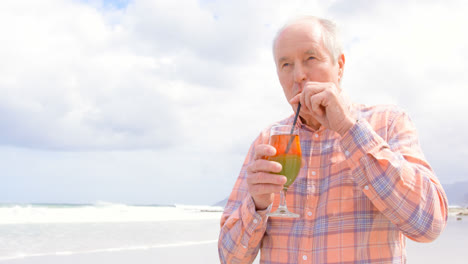 Front-view-of-old-caucasian-senior-man-drinking-cocktail-at-beach-4k