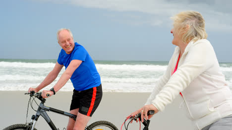 Side-view-of-old-caucasian-couple-riding-bicycle-at-beach-4k