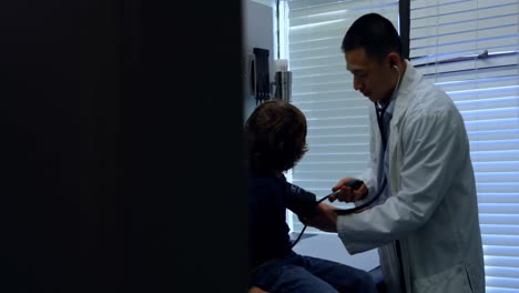 Side-view-of-young-asian-male-doctor-checking-blood-pressure-of-caucasian-boy-patient-in-clinic-4k