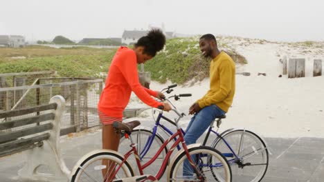 Side-view-of-young-black-couple-standing-with-bicycle-at-beach-on-a-sunny-day-4k