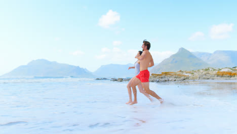 Side-view-of-young-caucasian-couple-running-with-hand-in-hand-at-beach-4k