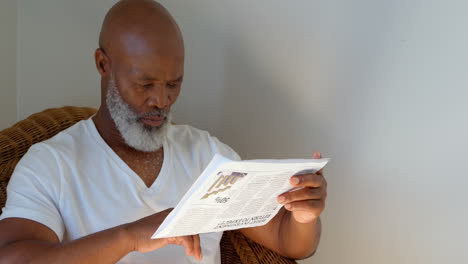 Front-view-of-black-mature-man-reading-newspaper-at-home-4k